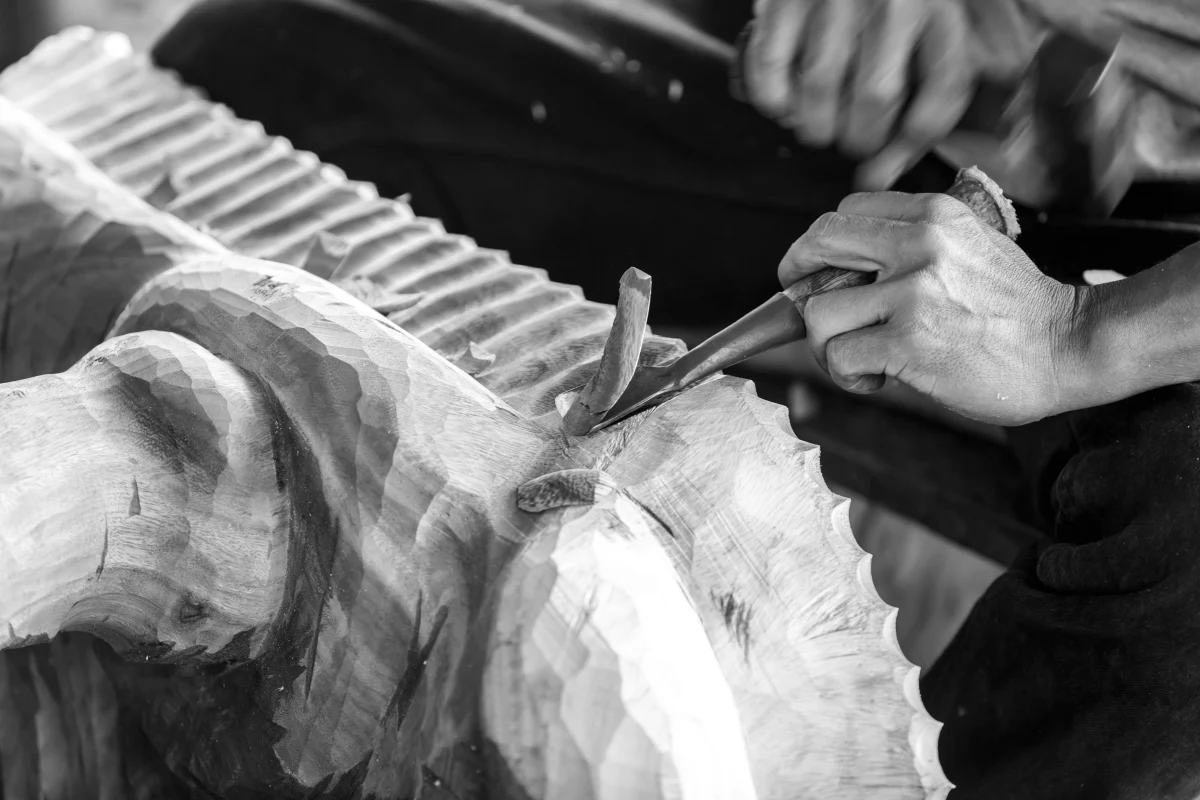 Artisan hands using traditional tools to carve a detailed wooden sculpture